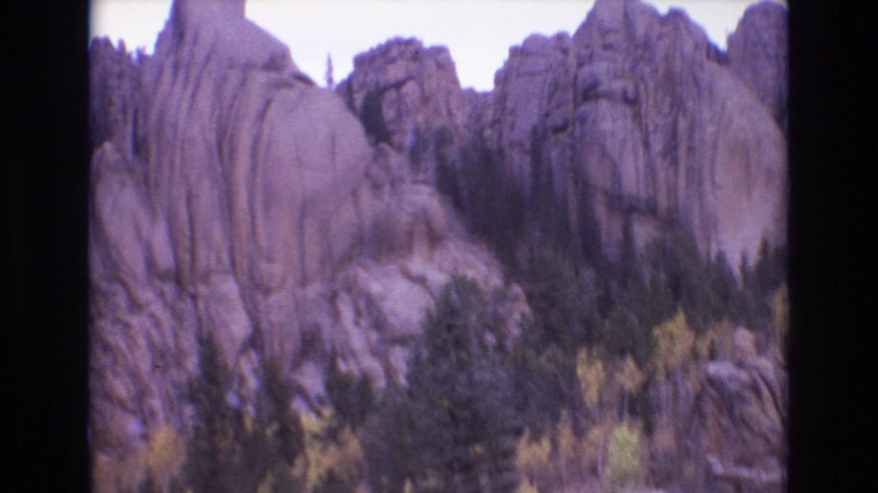 Rounded rock formations above pine trees and yellow-green foliage.