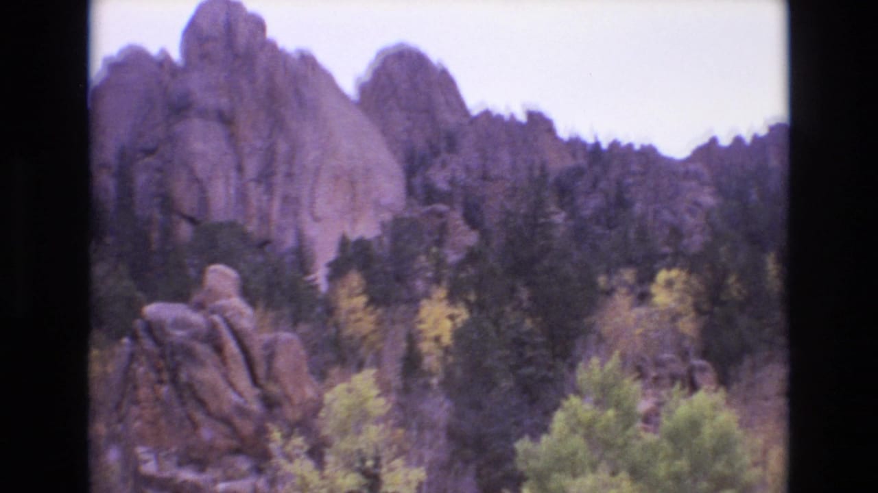 1973 Colorado Springs 8mm frame showing a rugged rock ridge, dark conifers, and yellowing deciduous trees on a mountain slope.