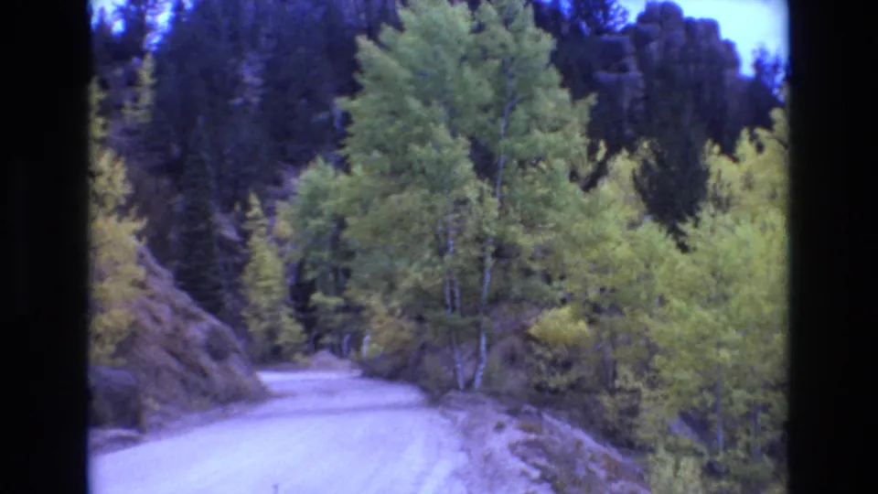A pale dirt road curves through aspens and evergreens below rocky slopes in Colorado Springs area home-movie footage from 1973.
