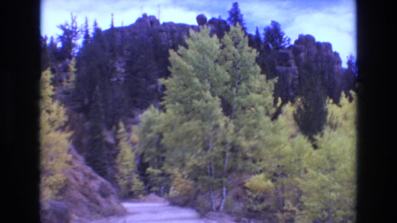 1973 8mm Colorado Springs footage showing an unimproved dirt road curving through green and yellow trees beneath a rocky mountain ridge.
