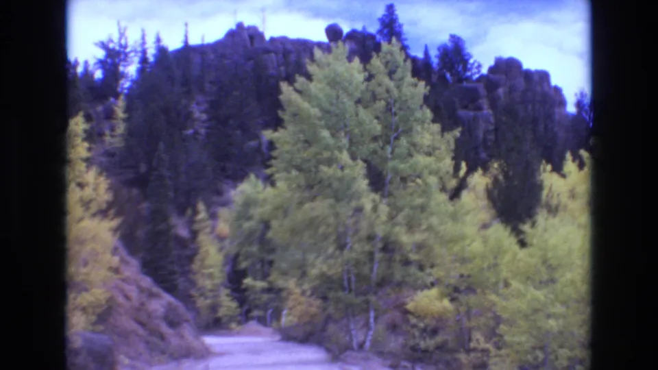 1973 8mm Colorado Springs footage showing an unimproved dirt road curving through green and yellow trees beneath a rocky mountain ridge.