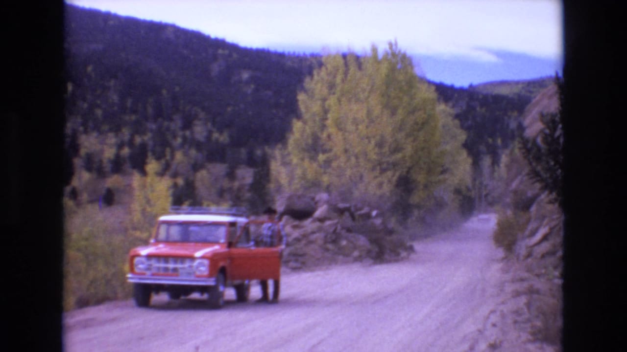 Red truck stopped on a dusty mountain road with a man beside the open door.