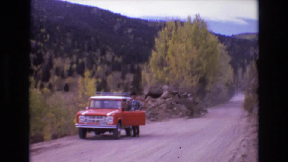Soft 8mm frame of an orange truck and a man beside its open door on a mountain dirt road near Colorado Springs in 1973.