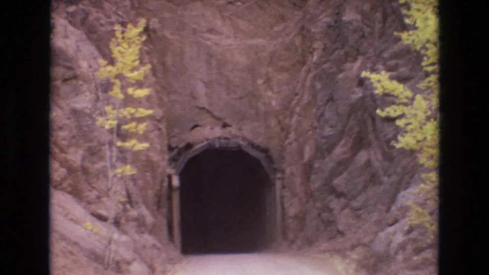 A dark tunnel entrance carved into a rocky hillside appears beside small yellow trees, consistent with the clip metadata describing a remote Colorado mountain setting.