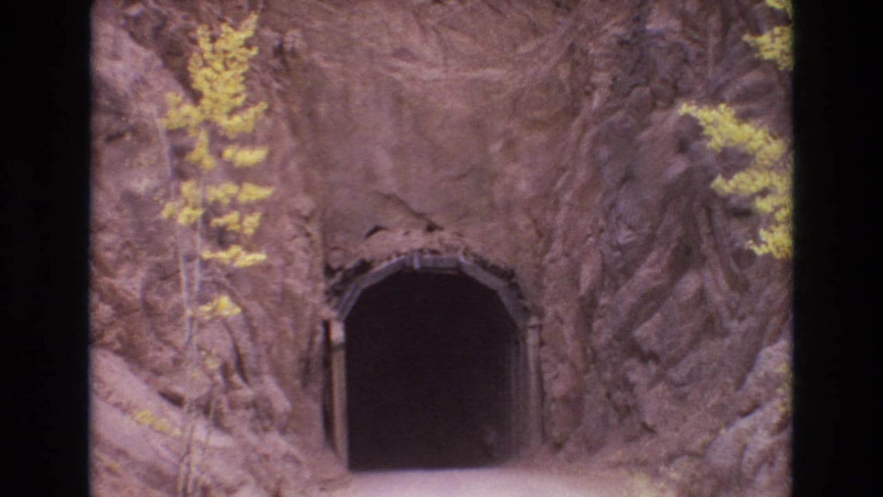 1973 Colorado Springs home-movie frame showing a dark arched road tunnel set into rough rock, with yellow-leafed trees and film borders visible.