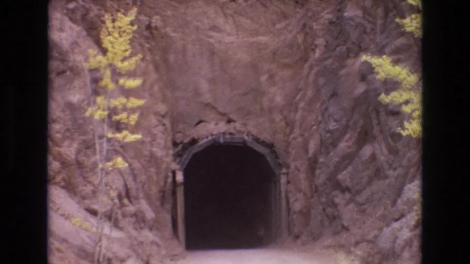1973 Colorado Springs home-movie frame showing a dark arched road tunnel set into rough rock, with yellow-leafed trees and film borders visible.