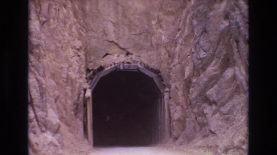 Home-movie still from the 1973 Colorado Springs clip showing the road-level approach to a dark tunnel beneath jagged rock.