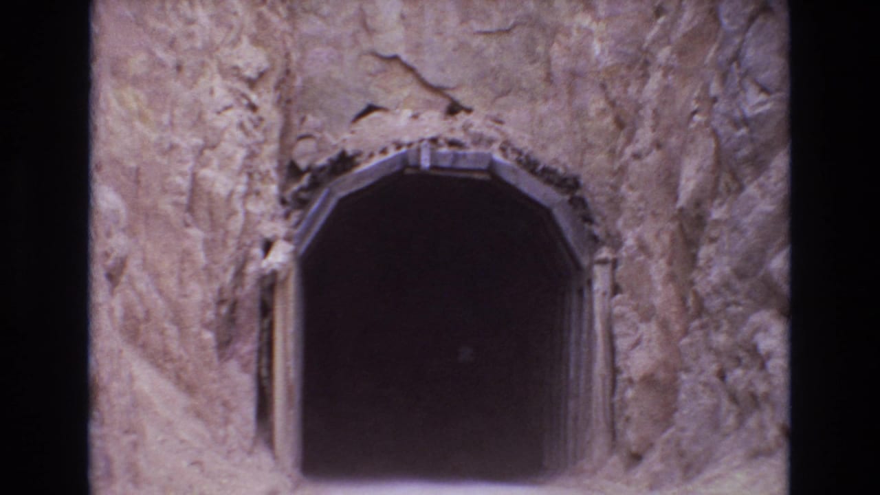 1973 Colorado Springs 8mm frame showing a dark arched mine-style entrance cut into rough tan rock with narrow wooden supports at the sides.