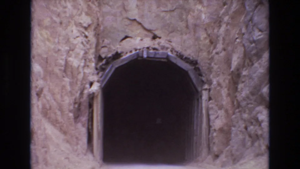 1973 Colorado Springs 8mm frame showing a dark arched mine-style entrance cut into rough tan rock with narrow wooden supports at the sides.