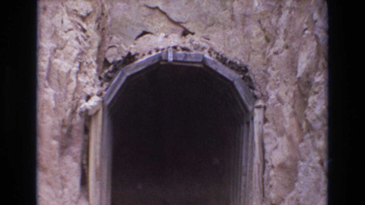 Closer view of a dark arched opening surrounded by rough rock.
