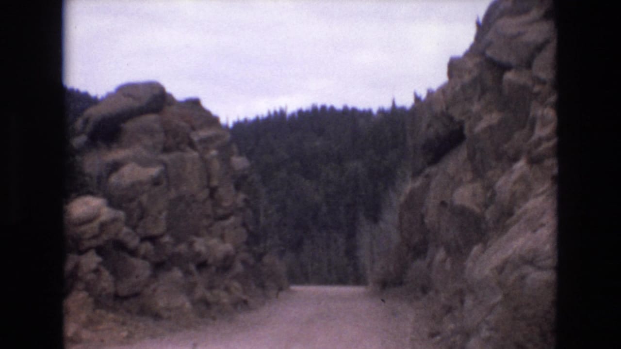 1973 Colorado Springs 8mm frame showing a pale dirt road entering a rocky canyon with dark pine forest ahead.