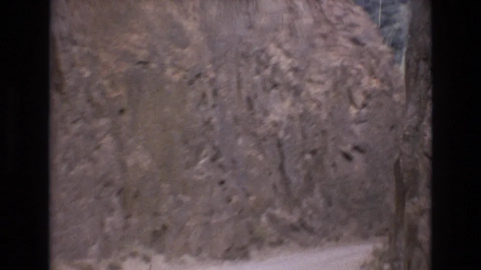 Close moving view of a rough rock cliff along the road in the Colorado Springs home-movie footage, with the frame dominated by textured stone and dark scan borders.