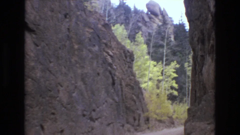 A narrow road runs between steep rock formations and trees, with bright foliage and dark evergreens visible in the Colorado Springs 8mm travel footage.