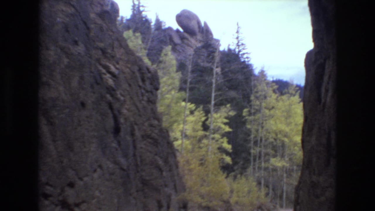 1973 8mm home-movie frame from the Colorado Springs area showing a rocky canyon edge, autumn trees, conifers, and distant hills under a pale sky.