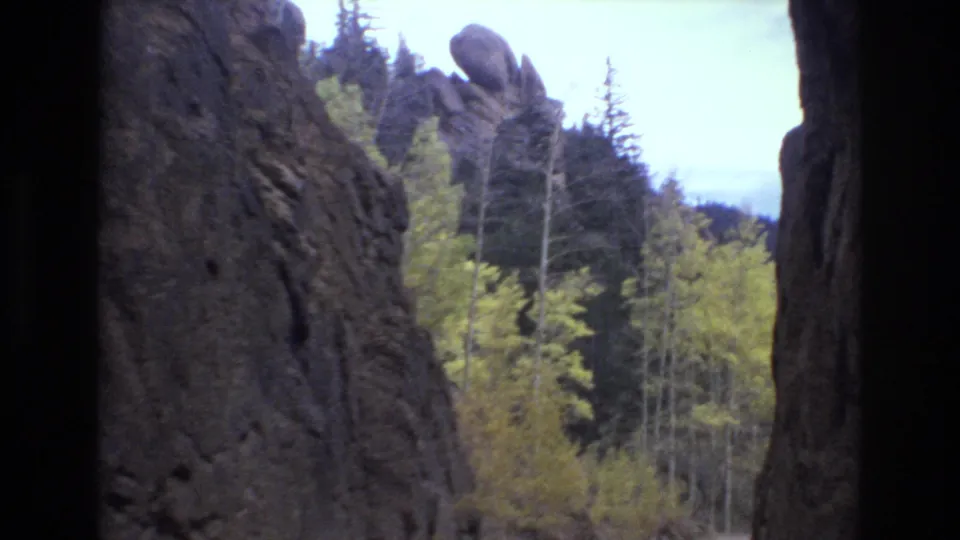 1973 8mm home-movie frame from the Colorado Springs area showing a rocky canyon edge, autumn trees, conifers, and distant hills under a pale sky.