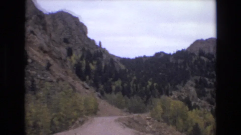 The dirt road leads toward a forested mountain valley near Colorado Springs, framed by rocky ridges and autumn-tinted trees in soft 8mm color.