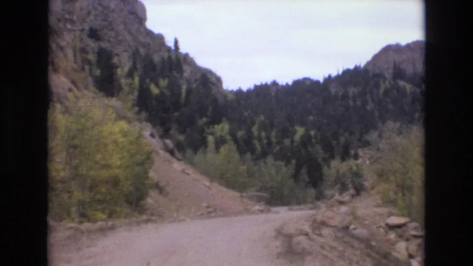 1973 8mm Colorado Springs frame showing the road bending through a rocky canyon with evergreen trees and yellow autumn brush.