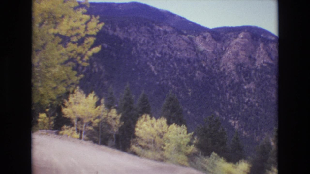 Winding dirt road with yellow trees and mountains in the background.