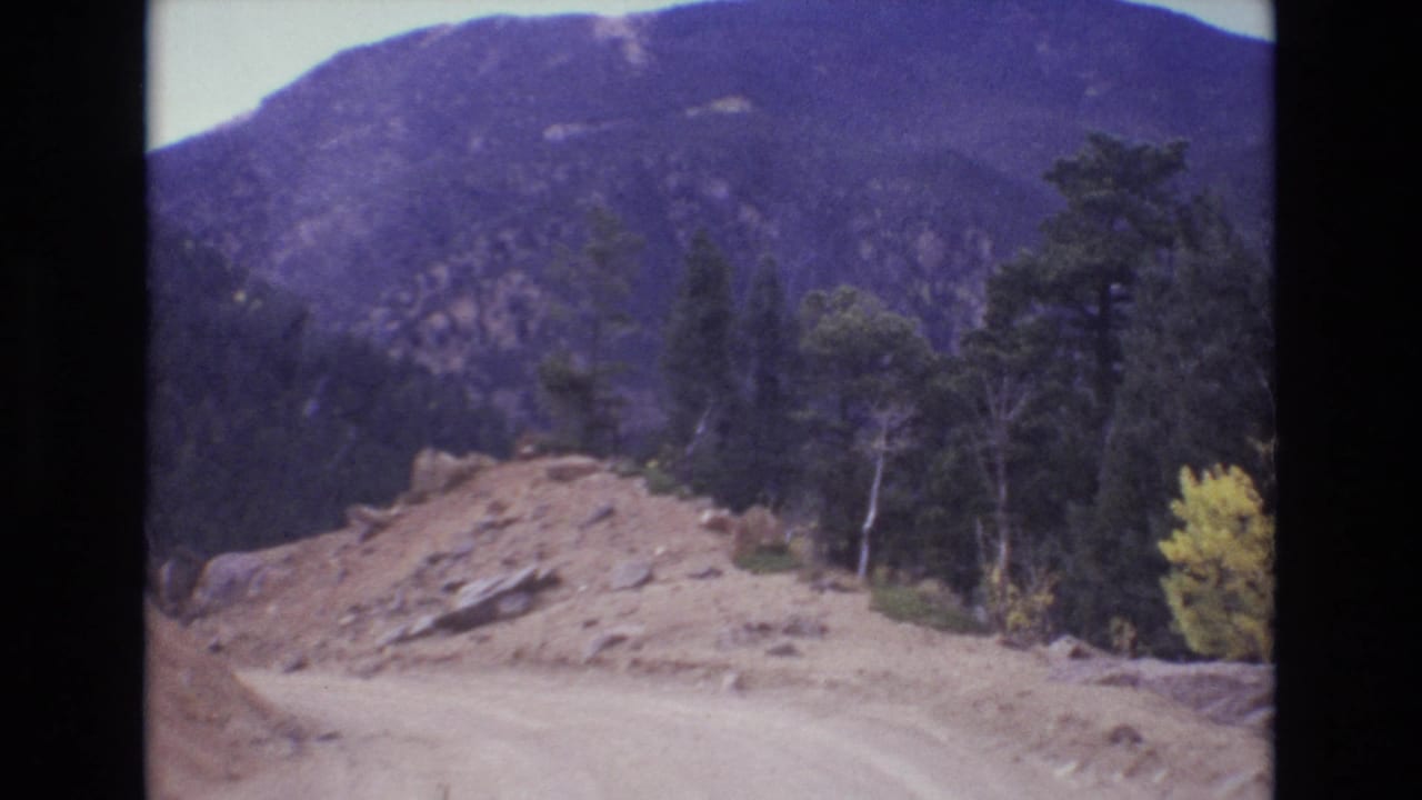 Unpaved road and gravel mound with forested mountain slopes in the background.