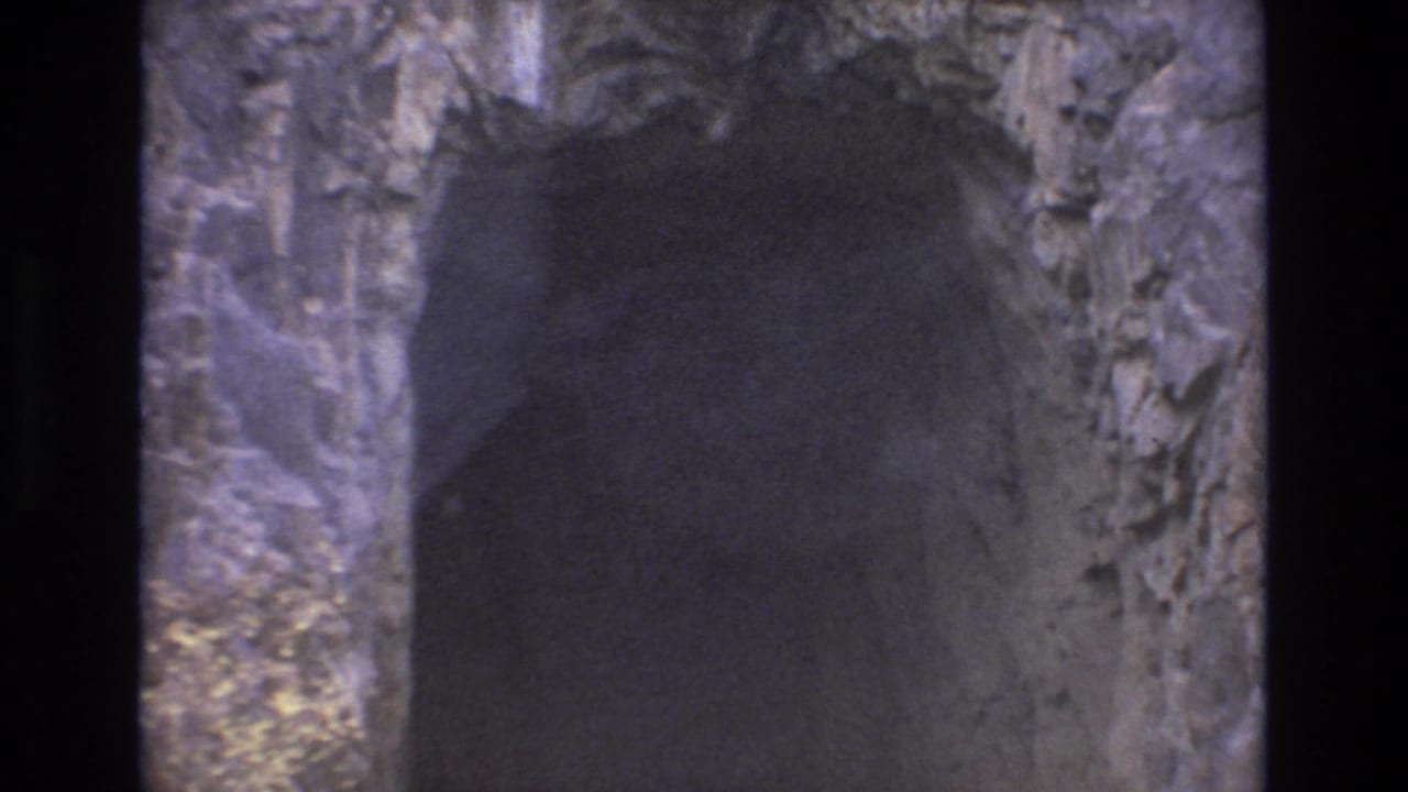 1973 Colorado Springs 8mm frame looking toward a shadowed cave opening, with uneven rocky walls and limited daylight around the passage.
