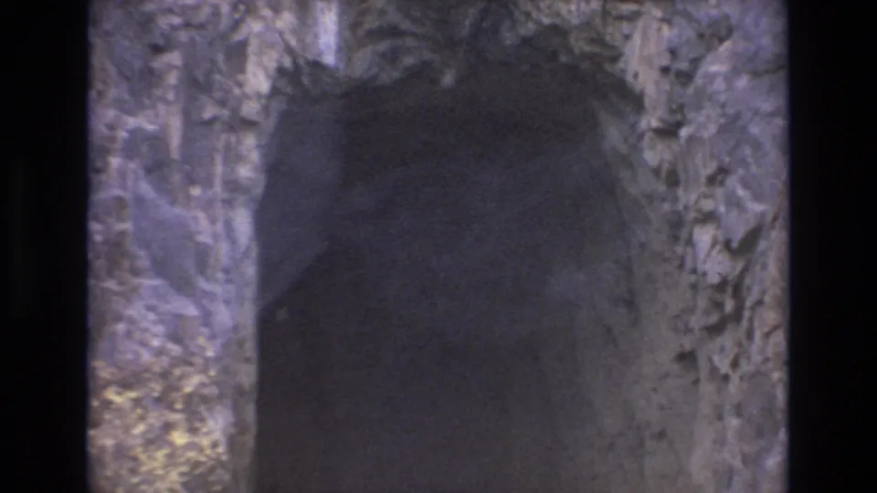 1973 Colorado Springs 8mm frame looking toward a shadowed cave opening, with uneven rocky walls and limited daylight around the passage.