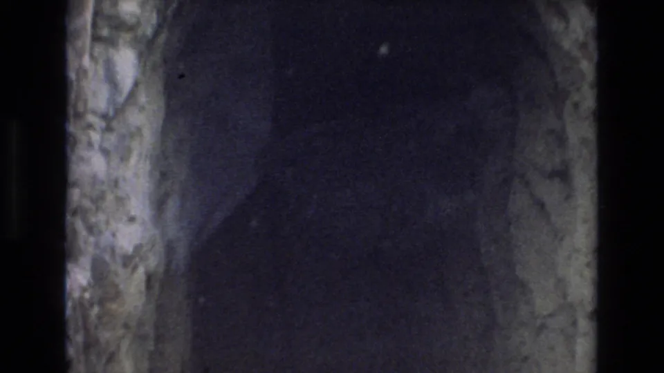 1973 Colorado Springs 8mm frame from inside or near the cave passage, showing rough stone surfaces fading into dark shadow.