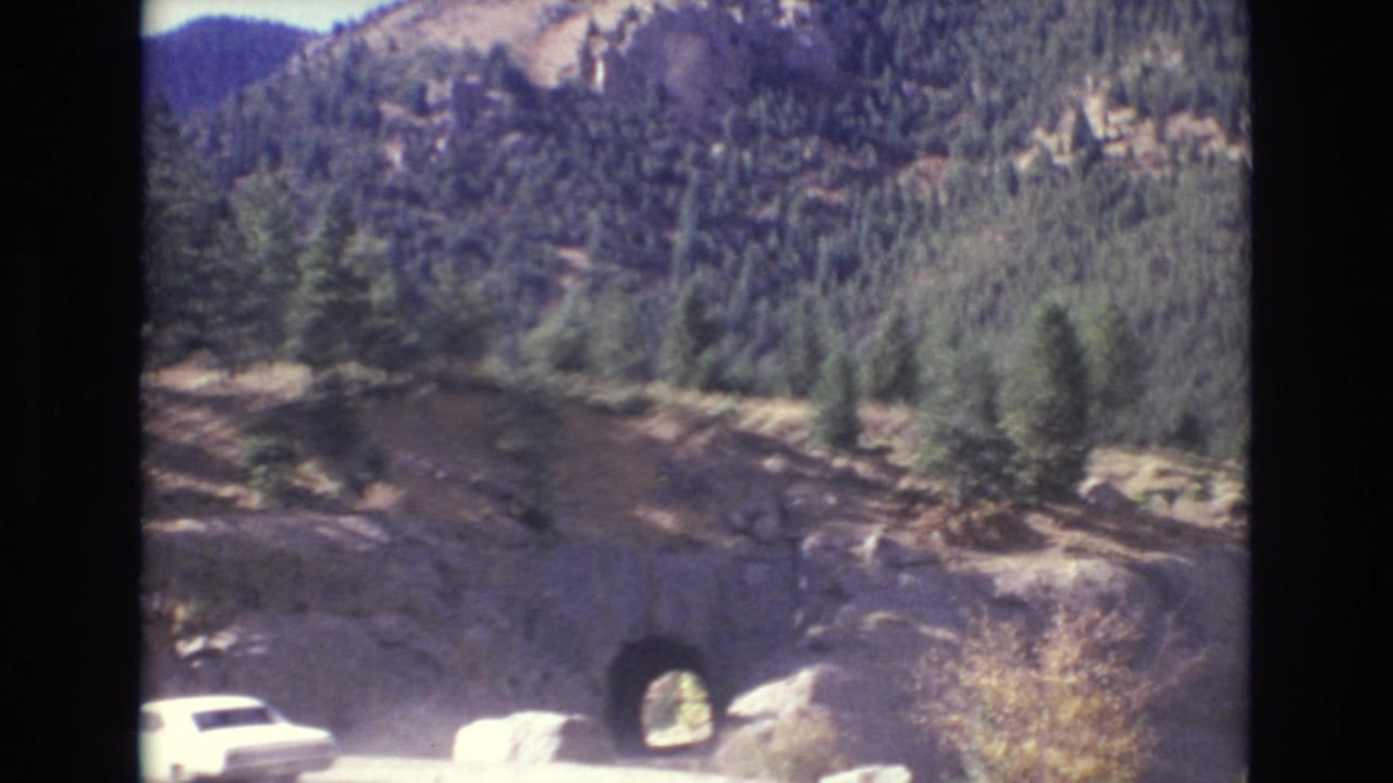 Mountain road approaching a small tunnel cut through rock.