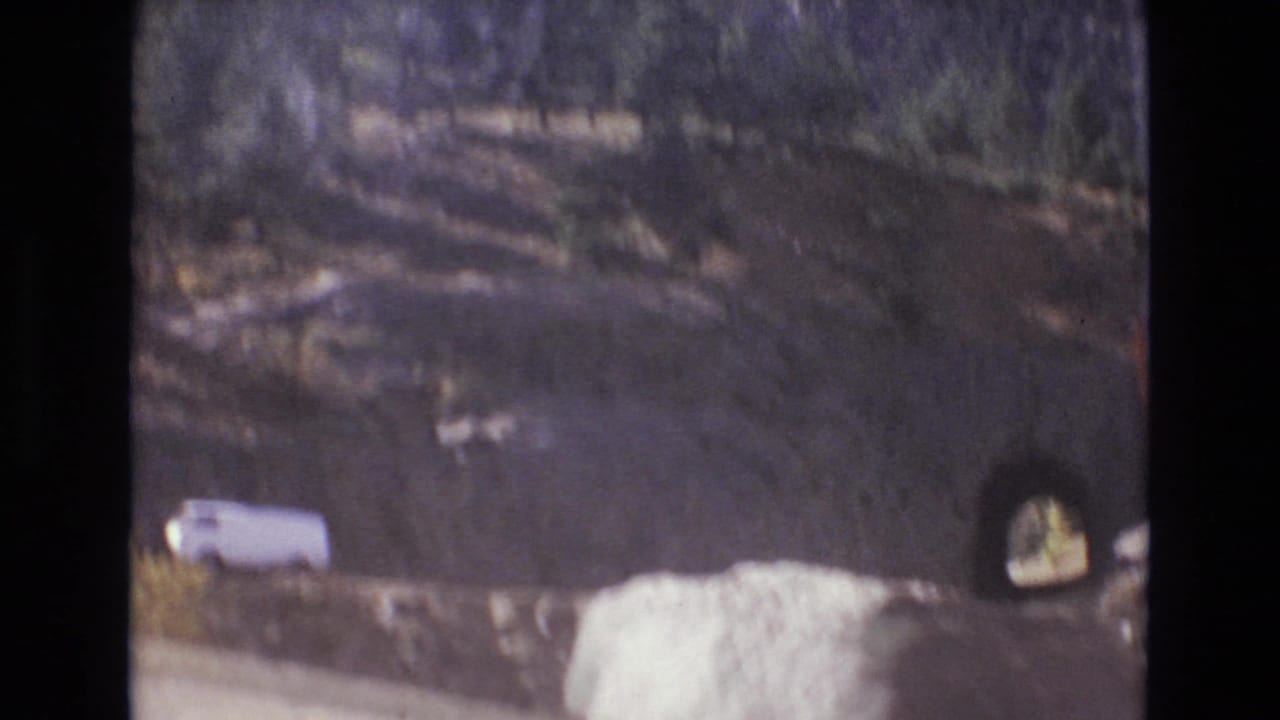 White van near a rocky roadside tunnel in mountain terrain.