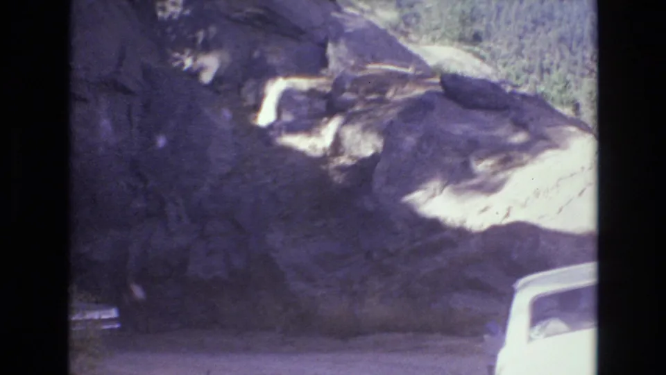 Final frame of the 1973 Colorado Springs-area road scene, with a rugged rock face and a partial white vehicle entering the lower right edge.