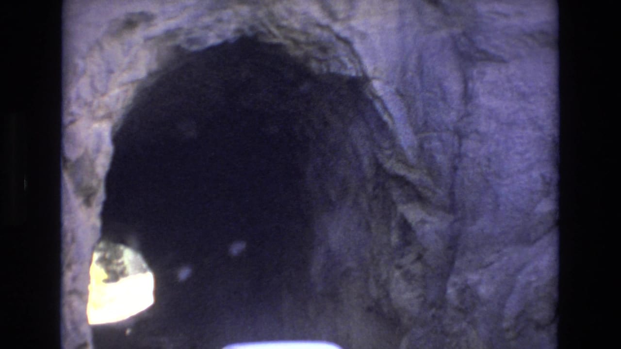 The camera frames a rough stone tunnel opening in Colorado Springs, with the tunnel interior falling into shadow and daylight visible at the far end.