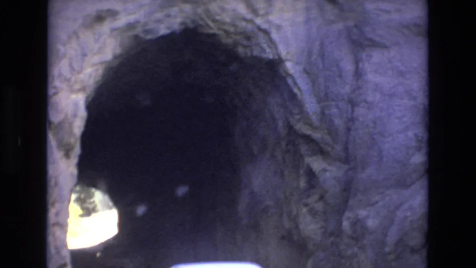 The camera frames a rough stone tunnel opening in Colorado Springs, with the tunnel interior falling into shadow and daylight visible at the far end.