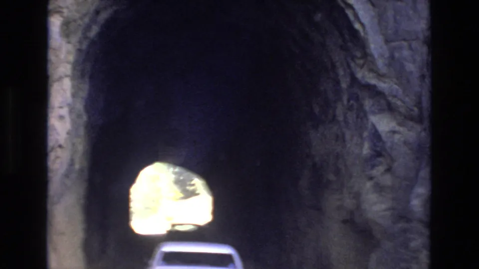 A pale car moves into the shadowed rock tunnel, with the bright far opening and rough tunnel wall visible in the 1973 Colorado Springs travel footage.