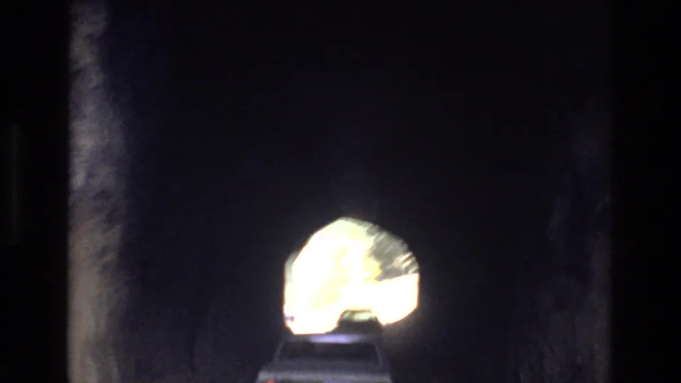 The vehicle is mostly inside the dark tunnel, with its roofline silhouetted below the bright exit opening in this short 8mm Colorado Springs road passage.