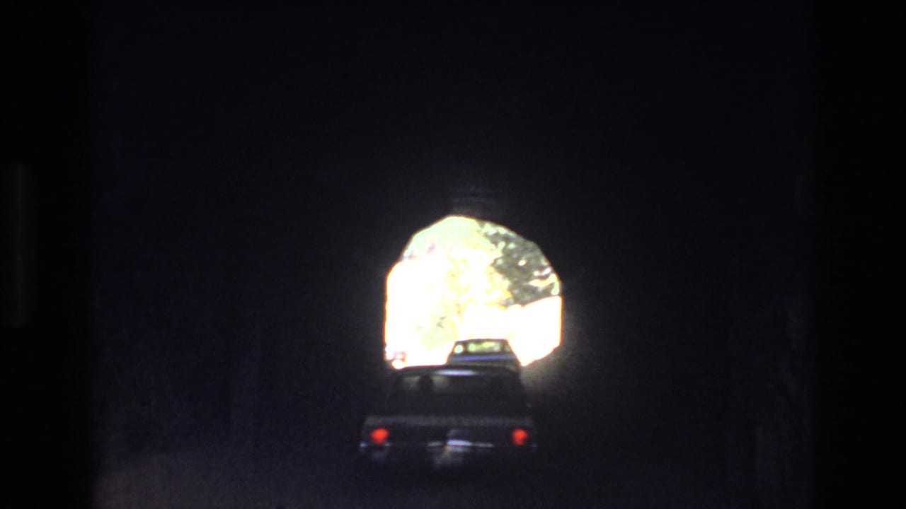 In supported 1973 Colorado mountain home-movie footage, a car is seen from behind inside a dark tunnel as daylight outlines the arched exit ahead.