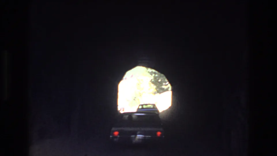 In supported 1973 Colorado mountain home-movie footage, a car is seen from behind inside a dark tunnel as daylight outlines the arched exit ahead.