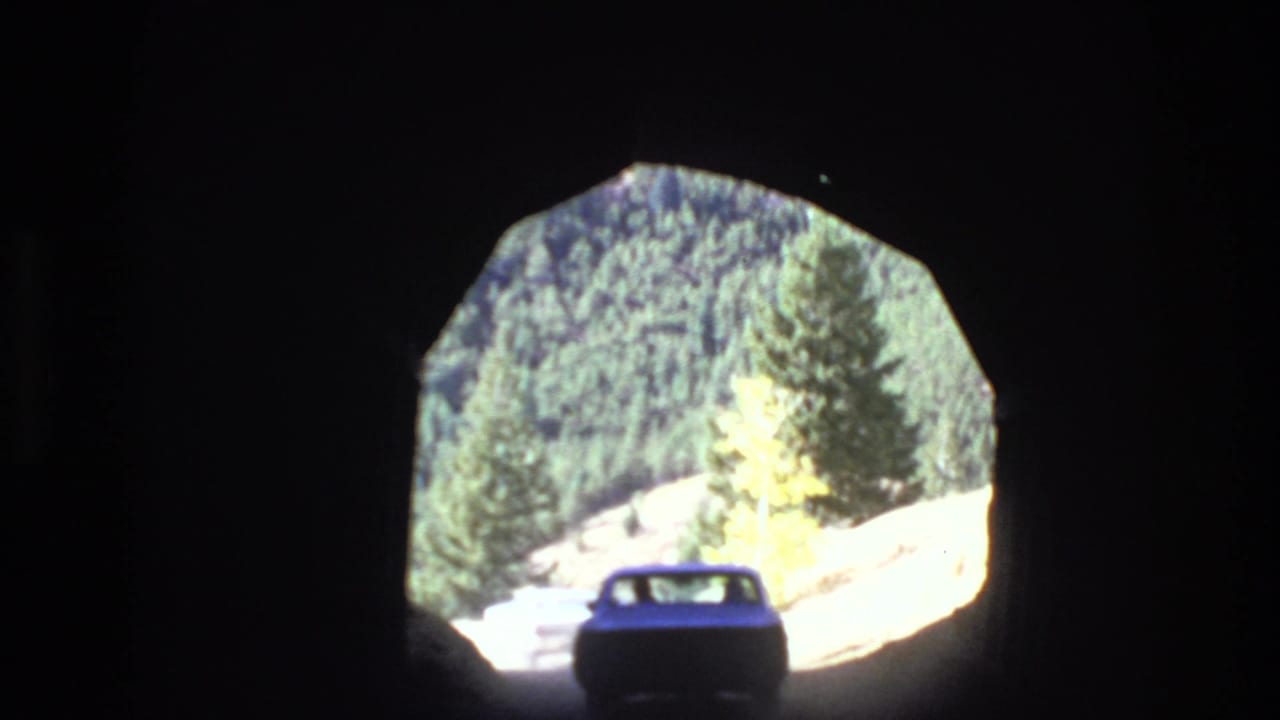 Car emerges toward a bright tunnel opening with forest visible outside.