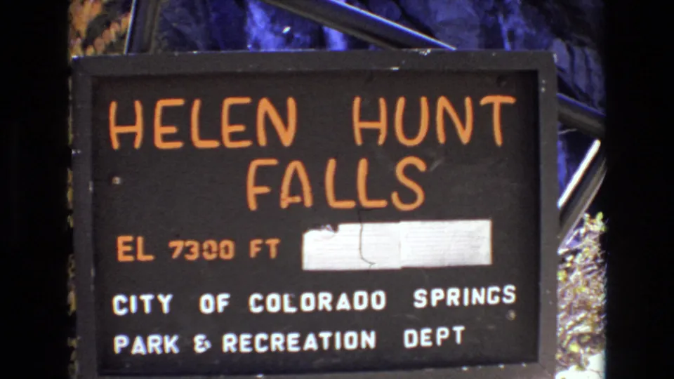 A close view of the Helen Hunt Falls sign shows the elevation marking and City of Colorado Springs Park and Recreation Department text in 1973 home-movie footage.