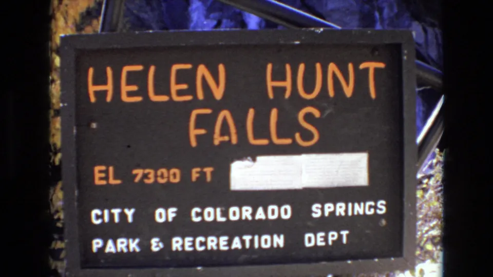 1973 Colorado Springs home-movie frame of the Helen Hunt Falls sign, showing the orange falls name, elevation 7300 ft, and City of Colorado Springs Park & Recreation Dept lettering.