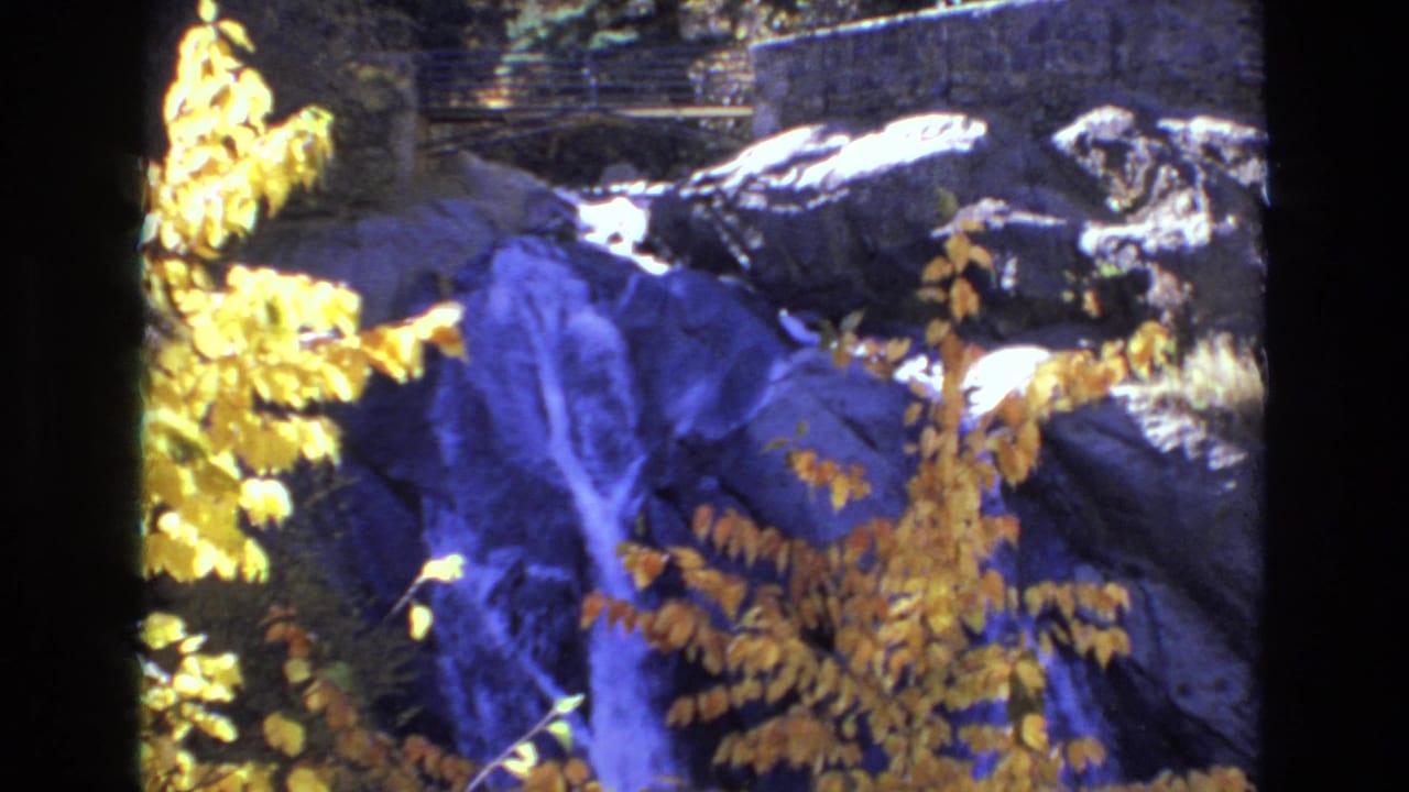 Waterfall over dark rocks framed by yellow leaves.