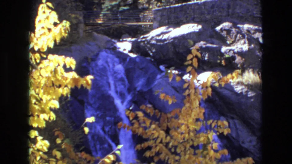 1973 8mm view of Helen Hunt Falls with yellow leaves partially obscuring the falling water and dark rock surface.