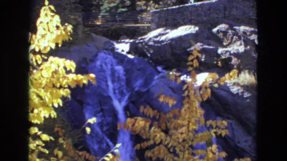 1973 8mm frame of Helen Hunt Falls with a soft view of water running over dark rock behind yellow autumn branches.