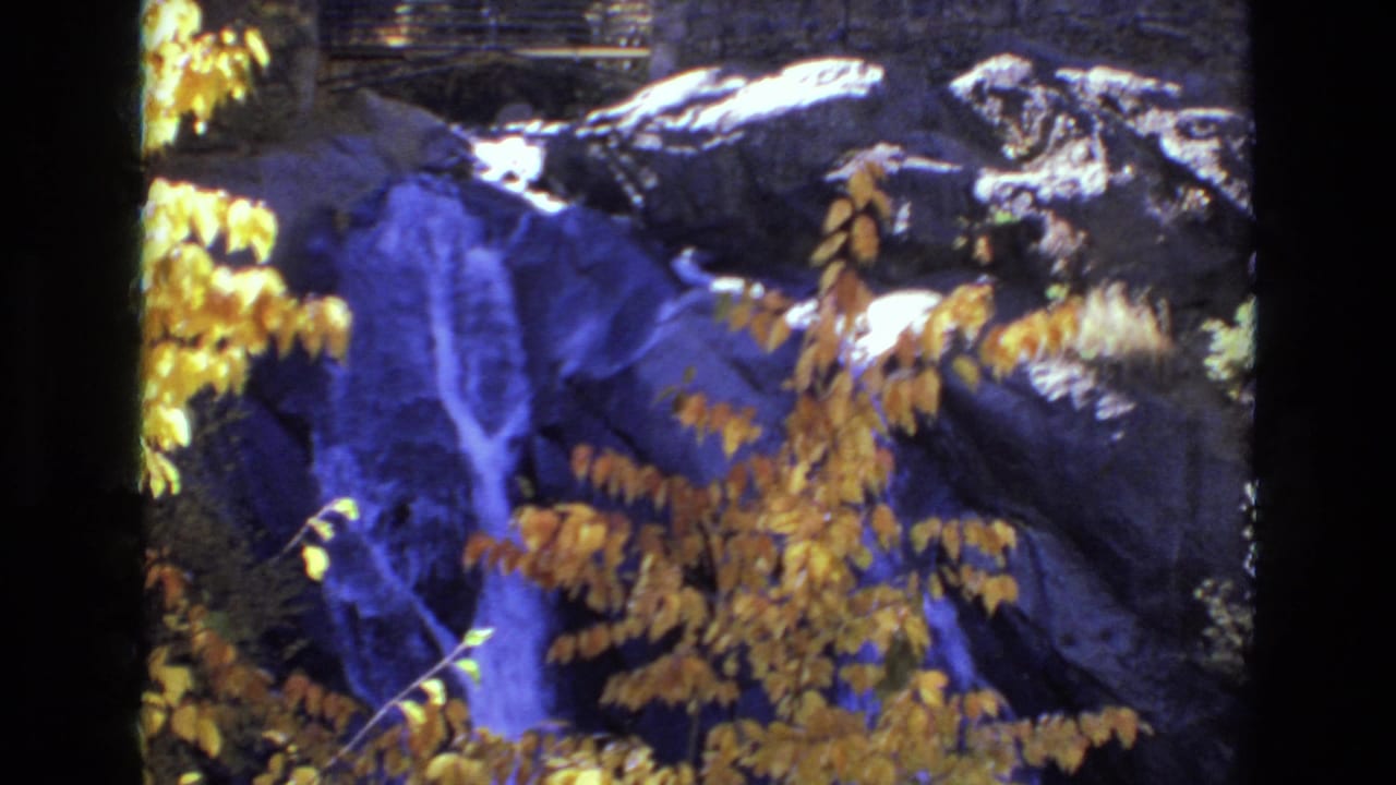 Rocky waterfall framed by golden leaves and dark stone.