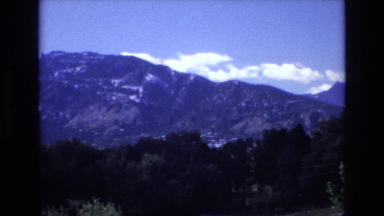 Mountain ridge beneath blue sky with trees in the foreground.