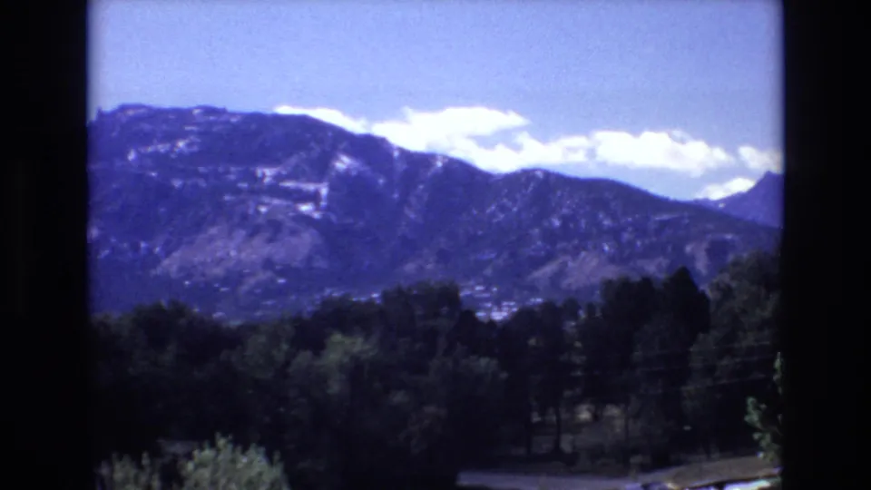 1973 Colorado Springs home-movie view of mountain slopes and clouds over a shaded tree line, with slight small-gauge film softness.