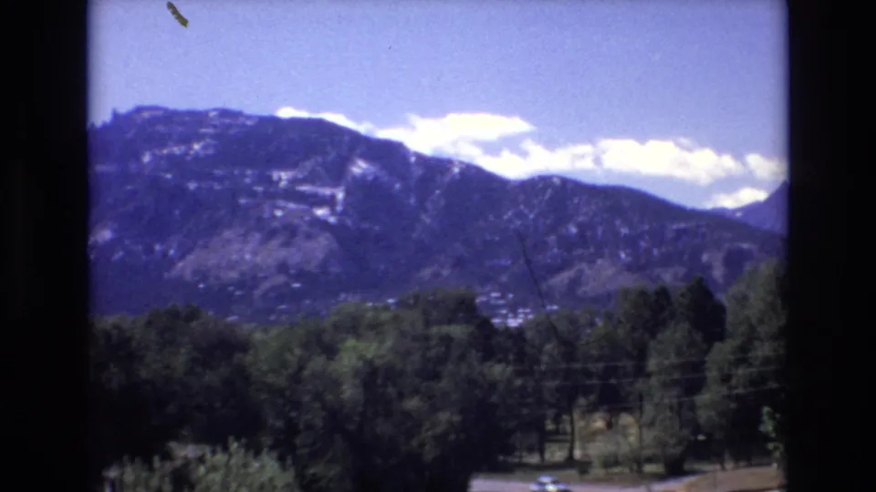 A final 1973 Colorado Springs frame keeps the mountain ridge and cloud bank centered, with green trees, slight dust marks, and dark 8mm borders visible.