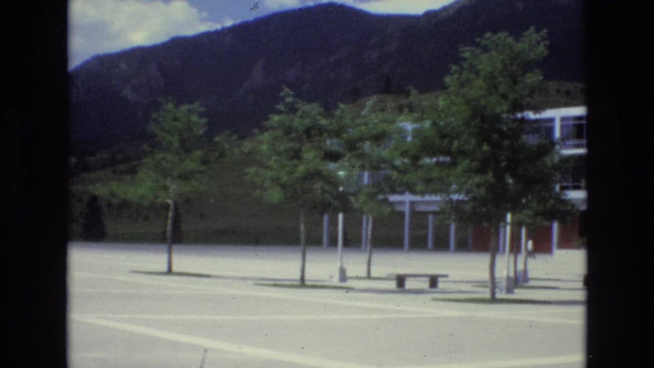 1973 Colorado Springs footage appears to show a modern glass-and-steel building across an open plaza, with young trees and dark mountain slopes behind it.