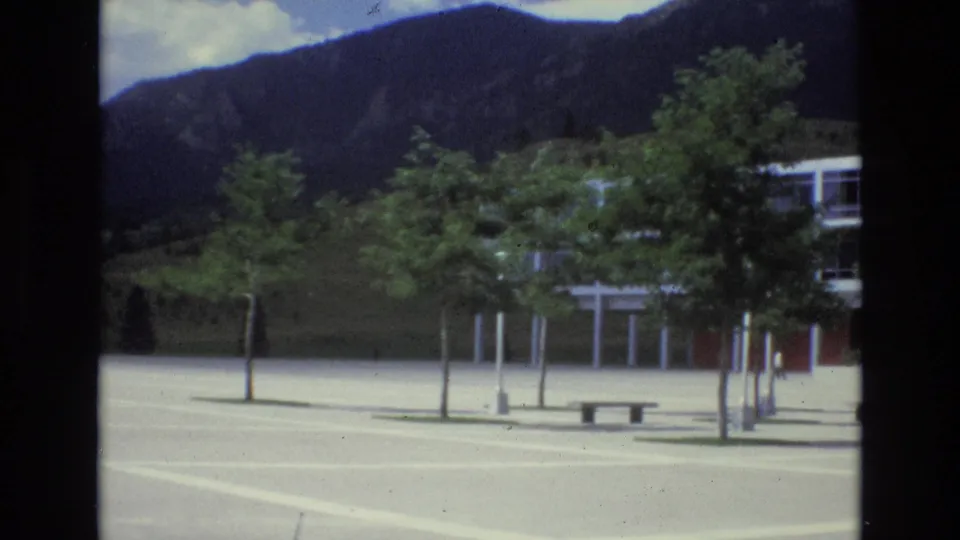 1973 Colorado Springs footage appears to show a modern glass-and-steel building across an open plaza, with young trees and dark mountain slopes behind it.