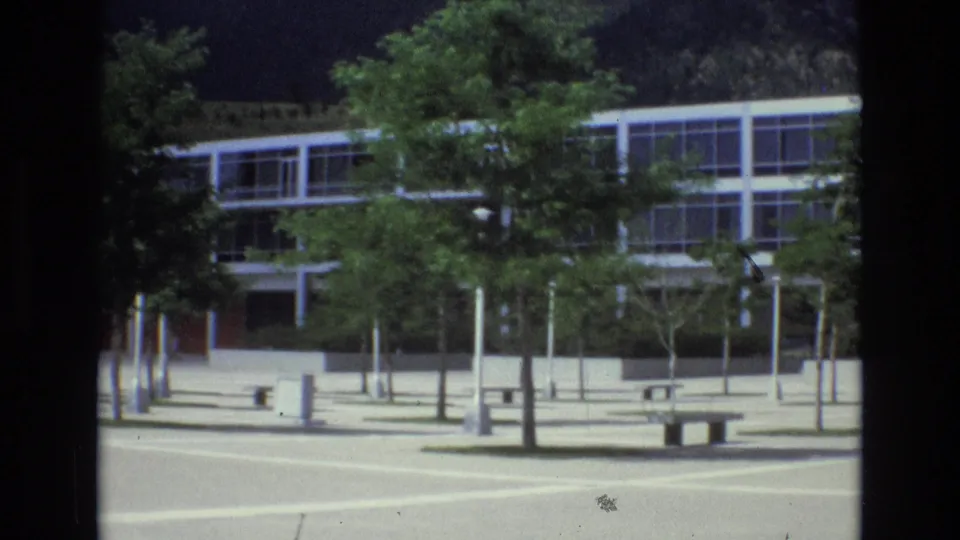 The final frame centers the glass-and-steel building behind plaza trees and benches, with the Colorado Springs mountain backdrop still visible above the roofline.