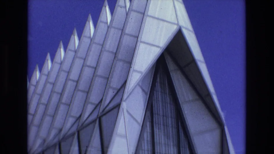 1973 Colorado Springs 8mm frame showing the United States Air Force Academy Chapel exterior from below, with repeated triangular spires and window panels against blue sky.
