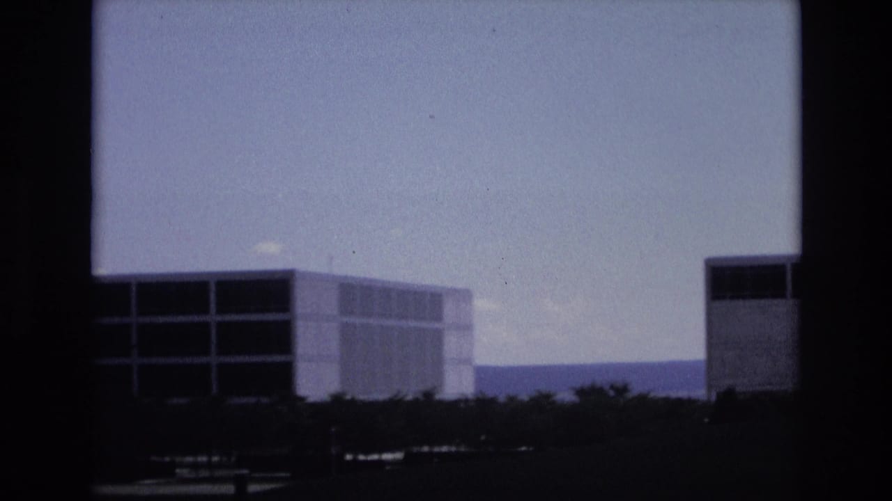 1973 Colorado Springs frame with a low, wide modernist building, horizontal window strips, trees at ground level, distant hills, and visible 8mm frame borders.